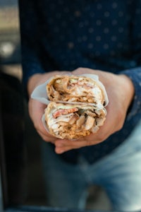 a man holding a burrito in front of a car